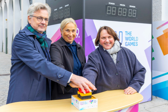 Die Countdown-Uhr auf dem Karlsruher Marktplatz wird feierlich gestartet. Von links: Dr. Frank Mentrup (Oberbürgermeister Karlsruhe & Präsident des Organisationskomitees), Anna Arzhanova (IWGA-Präsidentin), Theresa Schopper (Sportministerin Baden-Württemberg).